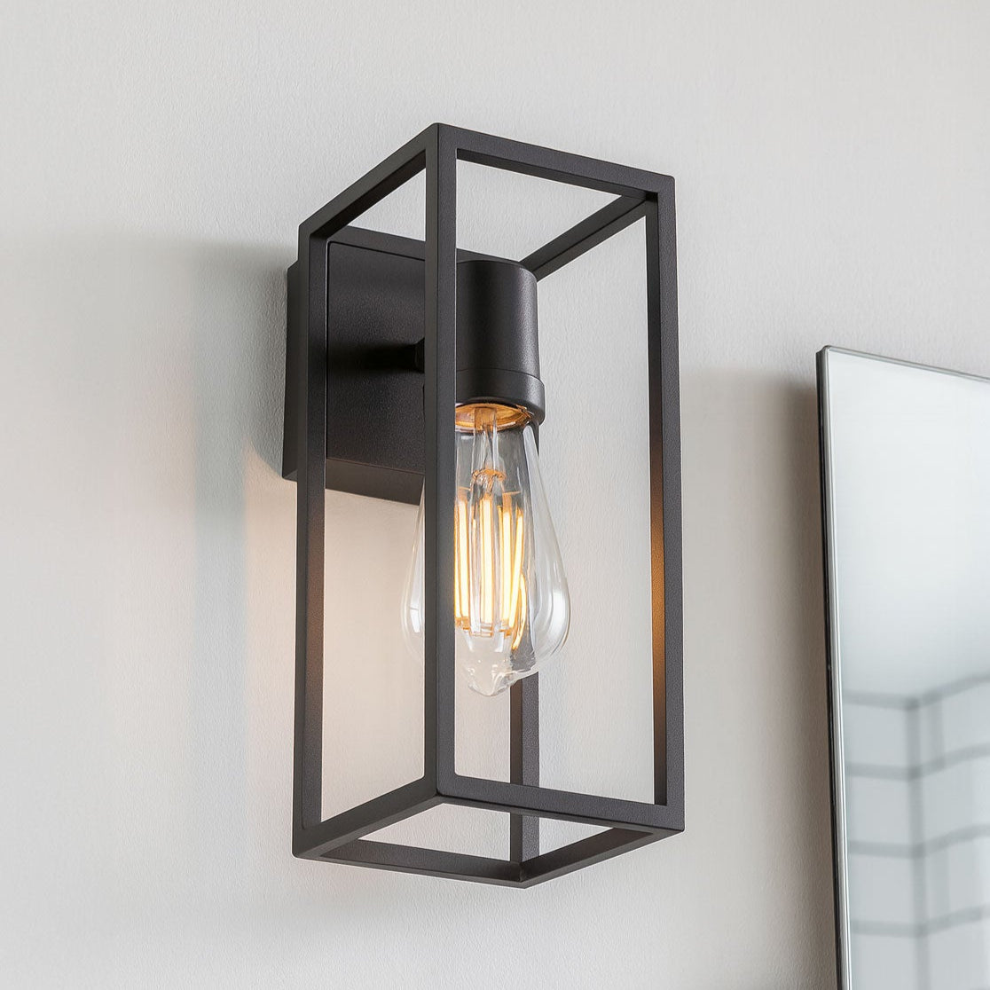 Modern black wall-mounted light fixture on a white wall with a mirror reflection.