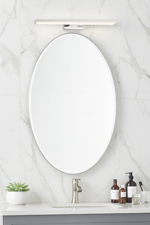 Bathroom vanity with oval mirror, sink, and toiletries on a marble wall background