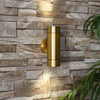 Illuminated brass up and down light on outdoor stone wall.