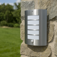 Outdoor wall light fixture on a stone wall with grass and trees in the background
